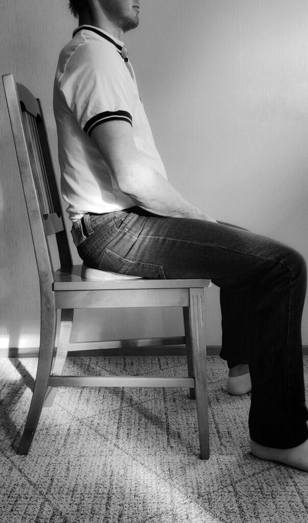 Mies istuu puisella tuolilla luupuu istuimen päällä ja hänen selkärankansa ja hartiansa on suorassa.  Säilyttäen selkärangan luonnollisen kaaren